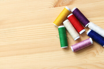 Fototapeta na wymiar Spools of thread of different colors, top view. Set of various colorful sewing threads on a wooden table, close-up. Sewing