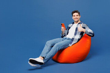 Full body young man he wear shirt white t-shirt casual clothes sit in bag chair hold in hand use...