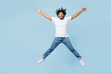 Full body young excited happy Indian man he wear white t-shirt casual clothes jump high with outstretched hands isolated on plain pastel light blue cyan background studio portrait. Lifestyle concept.