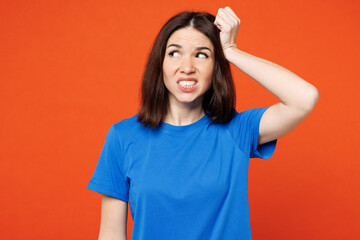 Young sad puzzled mistaken upset woman she wearing blue t-shirt casual clothes look aside on area mockup scratch hold head isolated on plain red orange background studio portrait. Lifestyle concept.