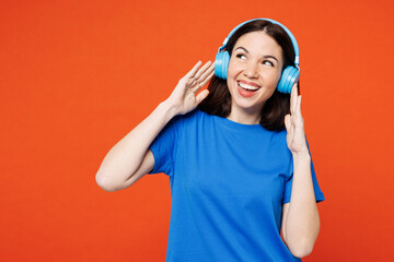 Young smiling cheerful fun cool happy woman wear blue t-shirt casual clothes listen to music in headphones look aside on area isolated on plain red orange background studio portrait Lifestyle concept