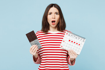 Young shocked sad woman wears red casual clothes eat sweet chocolate bar hold female periods pms...