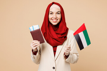 Traveler Asian Muslim woman wear red abaya hijab hold passport ticket UAE flag isolated on plain beige background Tourist travel abroad in free spare time rest getaway Air flight trip journey concept
