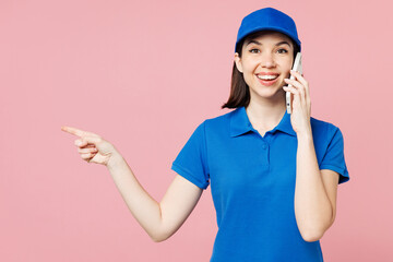 Professional delivery girl employee woman wear blue cap t-shirt uniform workwear work as dealer courier hold use mobile cell phone point finger aside isolated on plain pink background Service concept