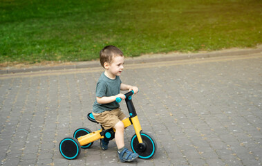 A smiling toddler boy of two or three years old rides a bicycle or balance bike in a city park on a...