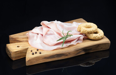 Mortadella ham, rosemary, black pepper and rustic taralli served on wooden cutting board. Black background