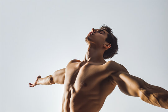 Dynamic portrait of shirtless male dancer posing with arms extended head tilted back against white studio background. Concept of human motions, wellness, natural beauty of male body.