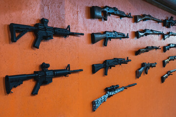 Firearms, rifles and shotguns on an orange wall in a shooting range.