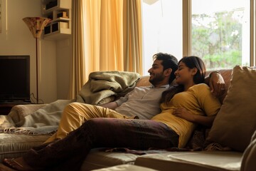 Cozy image of an Indian couple lounging on a couch, enjoying a relaxed moment together in a warmly lit living room