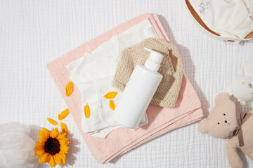 Daily baby care products for skin care or bathing with unlabeled bottle on pink bath towel, decorated by a sunflower and a brown bear. Blank space for adding designing elements, high angle shot
