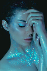 Beauty woman makeup with glitter on her body holding her hands to her face in a captivating pose