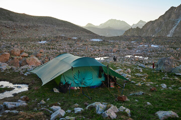 Solitary tent pitches amidst rocky terrain with a hiker strolling into the rugged wilderness at dawn
