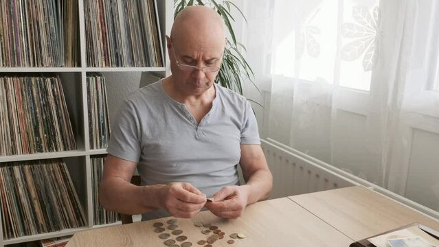 Senior man with reading glasses lays out euro cent coins on wooden table, counts meager cash money on table, Struggle for Survival, harsh reality of life in poverty
