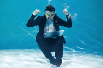 Artistic business concept. A man in a business style sits with a laptop underwater on a blue...