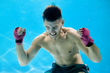 Artistic concept. Athletic man doing boxing with stress in water on blue background