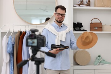 Smiling fashion blogger showing shoe and hat while recording video at home