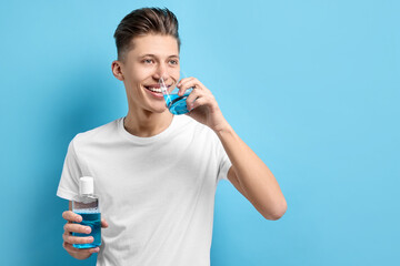 Young man using mouthwash on light blue background, space for text