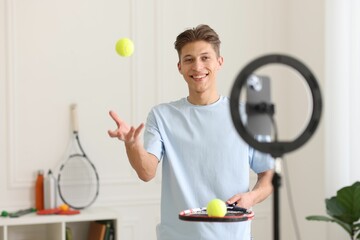 Smiling sports blogger with tennis racket and balls streaming online fitness lesson at home