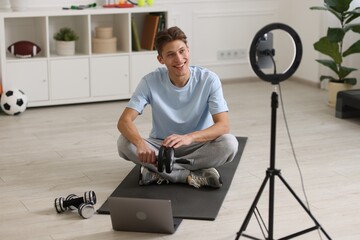 Fototapeta na wymiar Smiling sports blogger holding ab roller while streaming online fitness lesson with smartphone at home