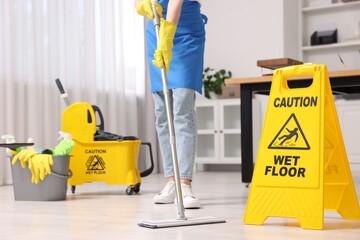 Cleaning service worker washing floor with mop, closeup. Bucket with supplies and wet floor sign in...