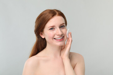 Naklejka premium Smiling woman with freckles wiping face on grey background