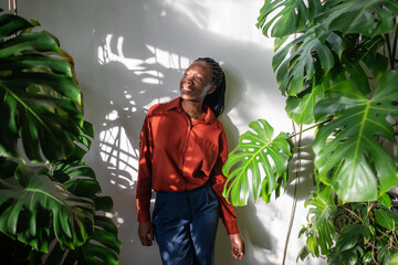 Relaxed African American woman stand in home garden enjoying houseplants. Carefree black female...