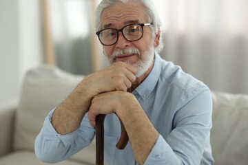 Portrait of grandpa with glasses and walking cane on sofa indoors