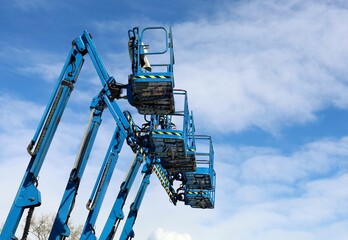 Five blue aerial work platforms of cherry pickers in a row against blue sky with clouds