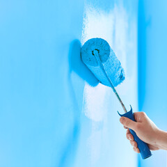 Close-up on the hand of a man who is painting a wall blue with a paint roller. Painting apartment, renovating with blue color paint
