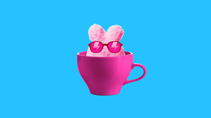 Pink bunny rabbit wearing sunglasses sitting inside cup on blue background. Contemporary art collage. Toy, accessories store, entertainment. Concept of surrealism, pop art, creativity, imagination.