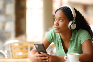 Black woman thinking listening audio with headphone and phone