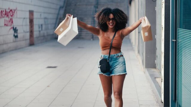 Video of happy smiling woman carrying shopping bags while walking through the city
