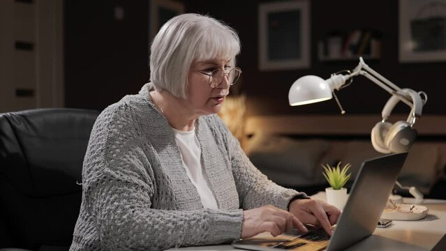 Senior woman learning to use computer. Mature woman unsure PC user with gray hair hesitates and clumsily tries to use laptop. Elderly woman mastering technology