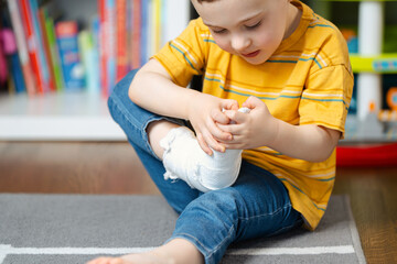 A little toddler boy holds his leg in a cast with his hands. Fracture of a foot and finger in children. Human healthcare and medicine concept. Bandage