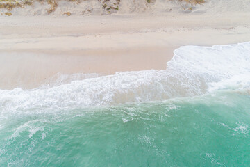 waves of a turquoise sea on the shore of a beach, aerial drone view