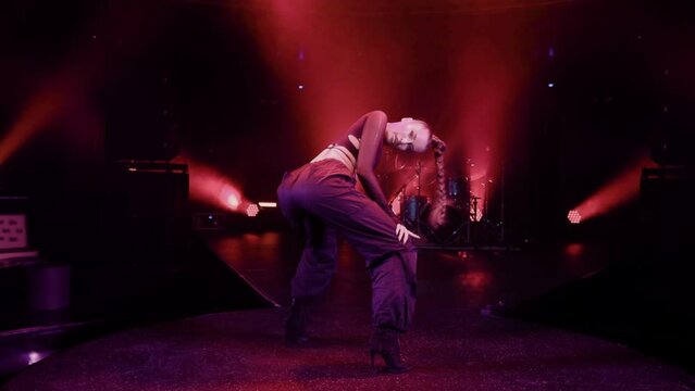 Slow movement camera captures a dancer in black pants and a long braid dancing on stage, bathed in concert lighting. Cozy club atmosphere.