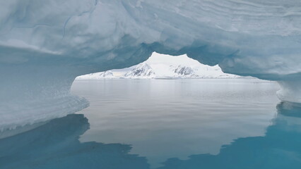 Antarctica Through Iceberg Arch. Snow Covered Mountains Background. Amazing View Of Mighty Polar...