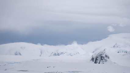Antarctic nature landscape with white snow covered mountain ranges at cloudy day. Wild winter untouched desert lands of Antarctica. Environment preserve and climate change scene