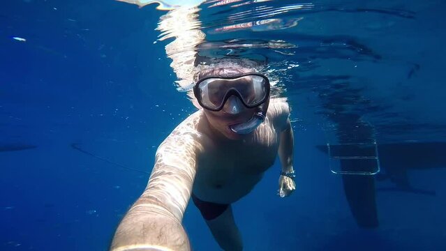 Diving with camera phone cencept: Man swimming in crystal blue water of the sea taking selfie while snorkeling. Underwater selfie.