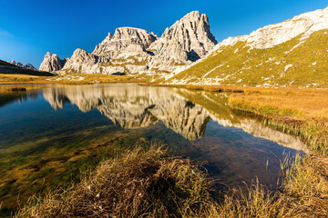 Mountain peaks of the Dolomites above the clear lake Laghi dei Piani with a reflection in the calm water surface during an early autumn sunny day with blue sky