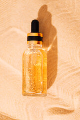 A mock-up glass bottle with a pipette with an intensive moisturizing concentrate with hyaluronic acid and vitamins on a background of sand.