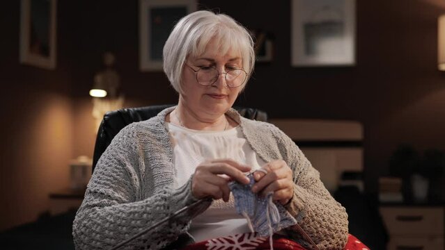 Knitting. Senior woman who looks like grandmother sits in chair and knits handmade item