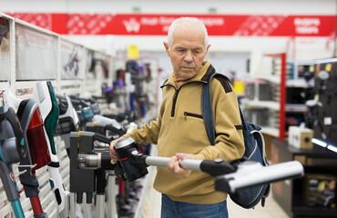 Senor man pensioner buying Upright Vacuum Cleaner in showroom of electrical appliance store
