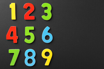 Colorful numbers on black background, flat lay. Space for text