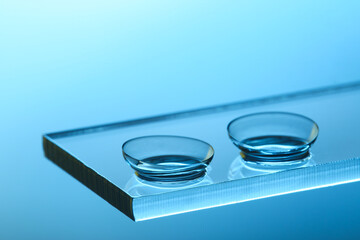 Obraz premium Pair of contact lenses on glass against light blue background, closeup