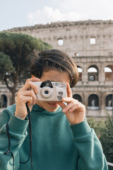 A girl in green sweater taking pictures with an old film camera, outside the Roman colosseum