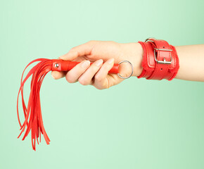 Woman's hand holding red whip for adult role play games over mint background