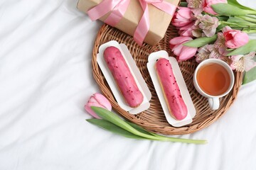 Tasty breakfast. Delicious eclairs, tea, flowers and gift box on bed, top view. Space for text
