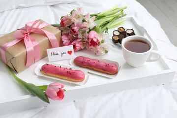 Tasty breakfast served in bed. Delicious desserts, tea, flowers, gift box and card with phrase I Love You on tray