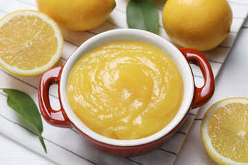 Delicious lemon curd in bowl and fresh citrus fruits on table, closeup
